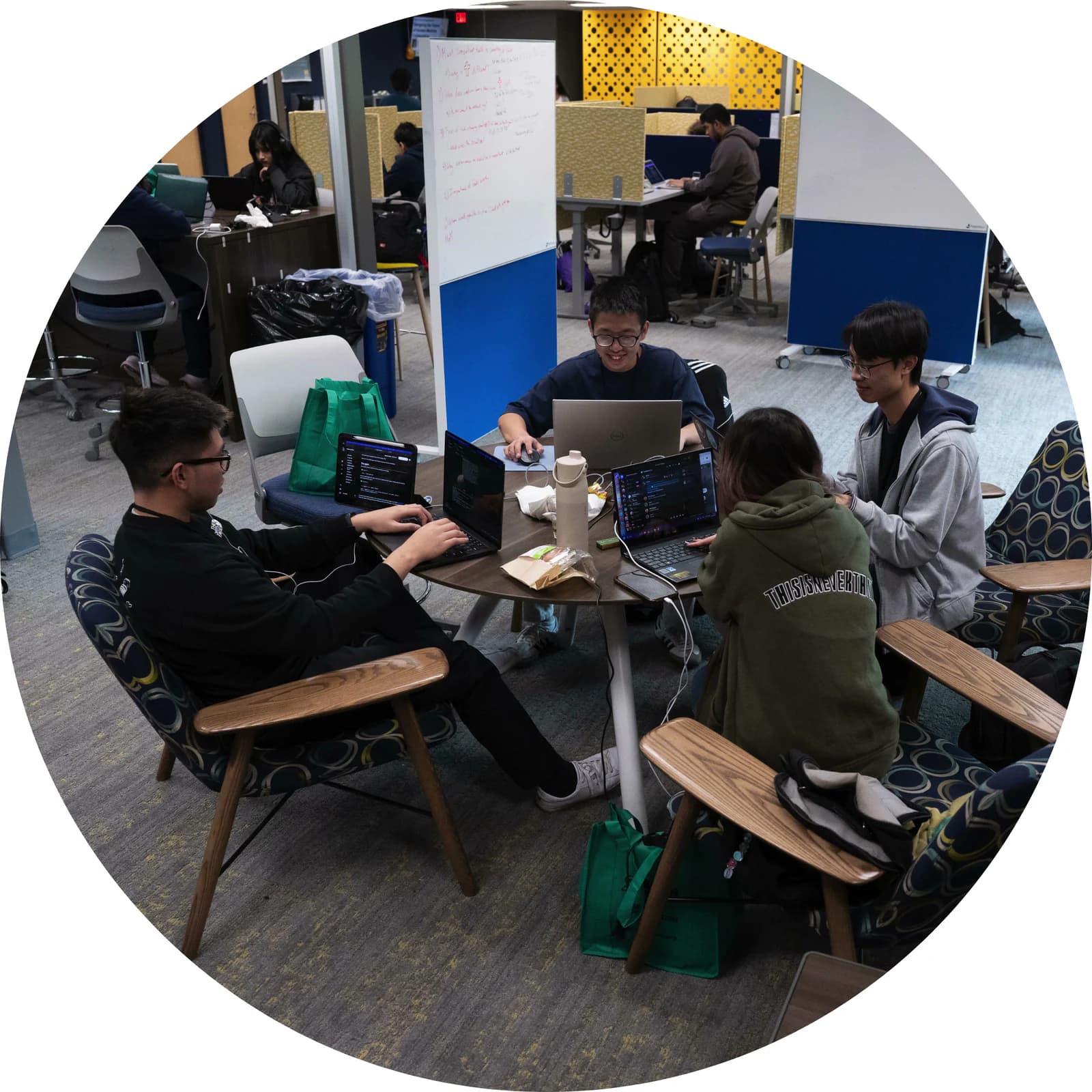 Hackers working on laptops around low tables in a campus commons